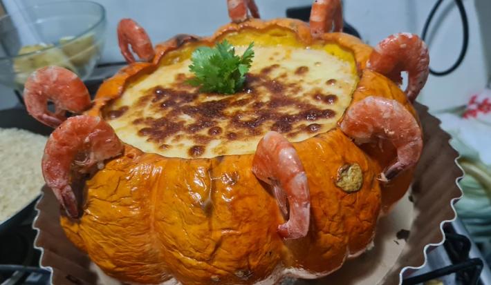 Foto da receita de camarão na moranga servida em uma moranga grande com camarões ao redor sobre uma base de torta de alumínio