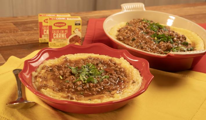 Fotografia mostra dois refratários vermelhos servidos com polenta e molho de carne por cima