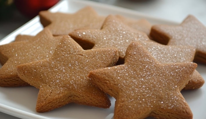 Em cima de uma mesa, prato redondo com biscoitos em formato de estrelas, decorados com açúcar cristal.