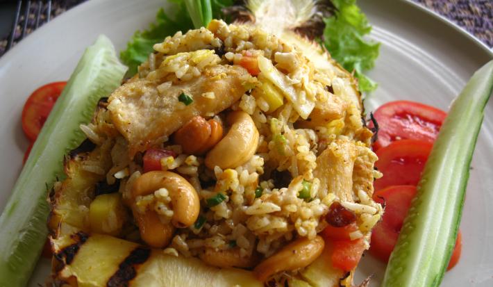 Fotografia de arroz com castanhas, com tomate e pepino decorando ao lado, dentro de um prato branco.