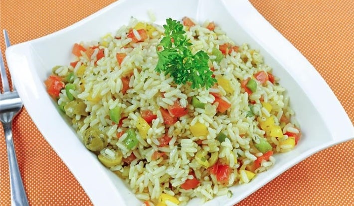 Em um prato branco, há arroz soltinho com uma mistura de legumes, como cenoura, ervilhas, milho, e pimentões, decorado com folhas de salsinha.