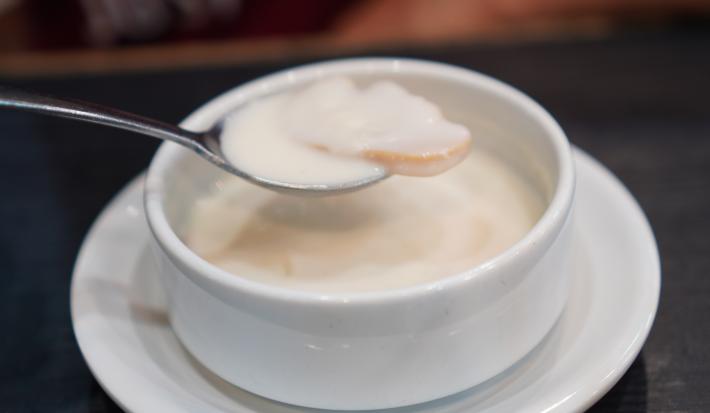 Fotografia de fatias de laranja cobertos por leite condensado dentro de um recipiente branco pequeno, sobre um prato branco pequeno.
