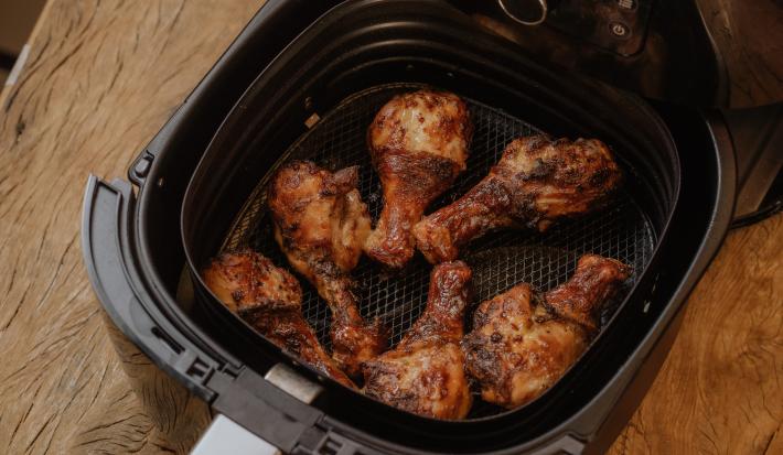 Fotografia em tons de marrom de uma bancada de madeira sobre ela o cesto da airfryer com 6 coxas de frango