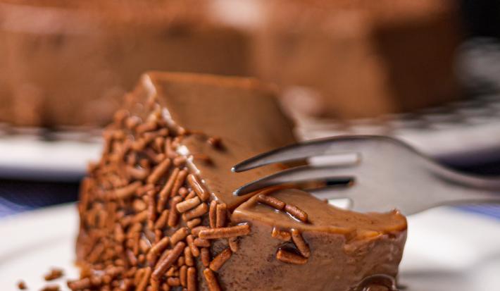 Foto da receita de Brigadeirão Sem Lactose. Observa-se uma fatia do Brigadeirão bem perto com chocolate granulado sendo cortada por um garfo.