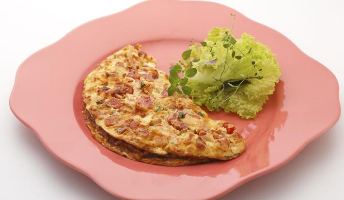 Foto de um prato rosa com um omelete em cima e algumas folhas de alface decorando