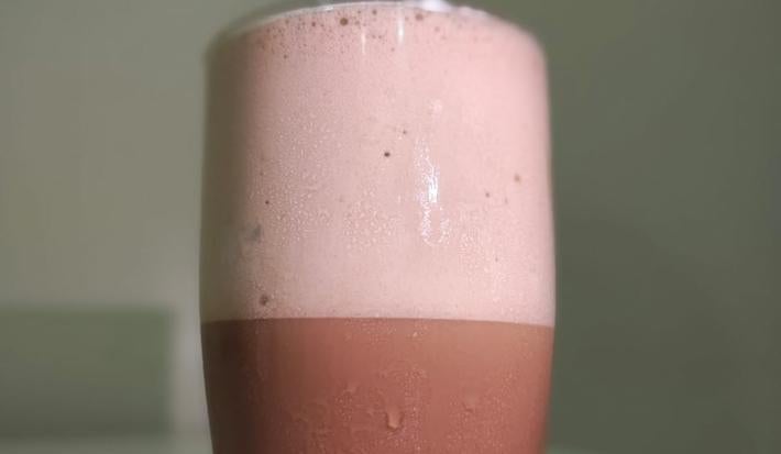 foto da receita de frappe com chocolate servida num copo de vidro alto sobre uma mesa branca