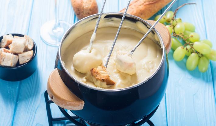 Foto da Receita de Fondue de Queijo Sem Lactose. Observa-se uma panelinha de fondue azul com três espátulas de pão dentro.