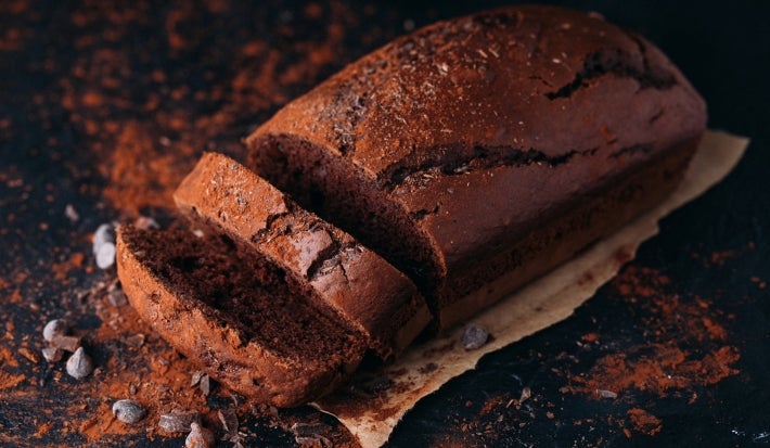Em cima de uma mesa, bolo de chocolate cortado em duas fatias, polvilhado com cacau em pó.