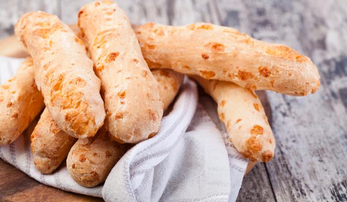 Fotografia em tons de cinza com uma toalha branca ao centro. Em cima da toalha existe vários biscoitinhos de polvilho dourados.