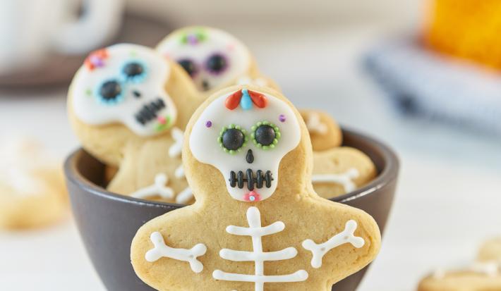 Imagem aproximada de um biscoito em formato de caveira com a decoração no tema de halloween, em uma bancada em tons claros