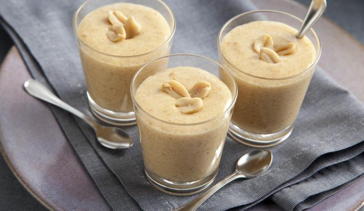fotografia em tons de bege e cinza de uma bancada cinza vista de cima. Contém 3 copinhos com o creme de paçoca com amendoim por cima para decorar e abaixo um pano cinza. fotografia em tons de bege e cinza de uma bancada cinza vista de cima. Contém 3 copinhos com o creme de paçoca com amendoim por cima para decorar e abaixo um pano cinza.