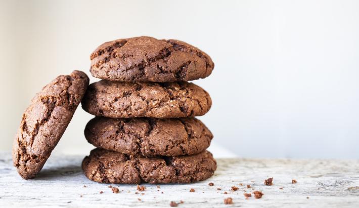 fotografia em tons de branco e marrom de uma bancada branca vista de frente. Contém 4 cookies de chocolate empilhados e um ao lado.