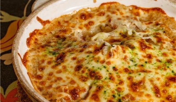 Em uma mesa, prato redondo com queijo gratinado, no meio do prato há um buraco com frango desfiado.