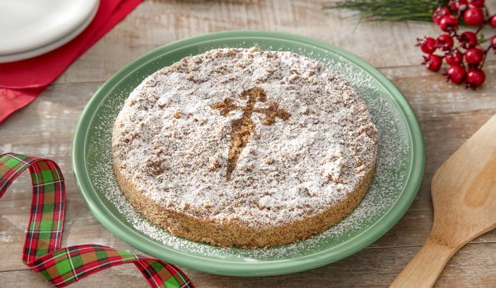Foto da receita de torta de santiago servida em um prato verde grande sobre uma mesa de madeira com decoração de natal e uma espátula de madeira ao lado