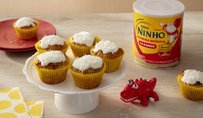 Fotografia em tons de amarelo e vermelho com 5 bolinhos ao centro. Por cima de cada bolinho existe um creme de leite de coco, coco ralado e NINHO Primeira Infância