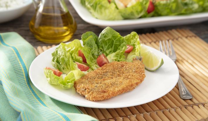 Imagem de um prato branco com um pedaço de sardinha frita com uma salada verde e um pedaço de limão.