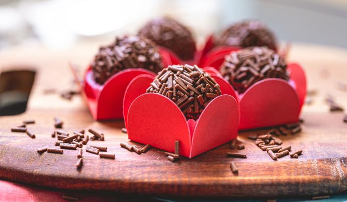 Imagem de brigadeiros cobertos com chocolate granulado na forminha vermelha sobre uma tábua de madeira.