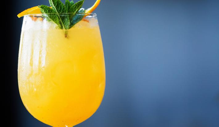 Foto da receita de G&T Wild, na cor em tom amarelada, servida numa taça de vidro e decorada com hortelã.
