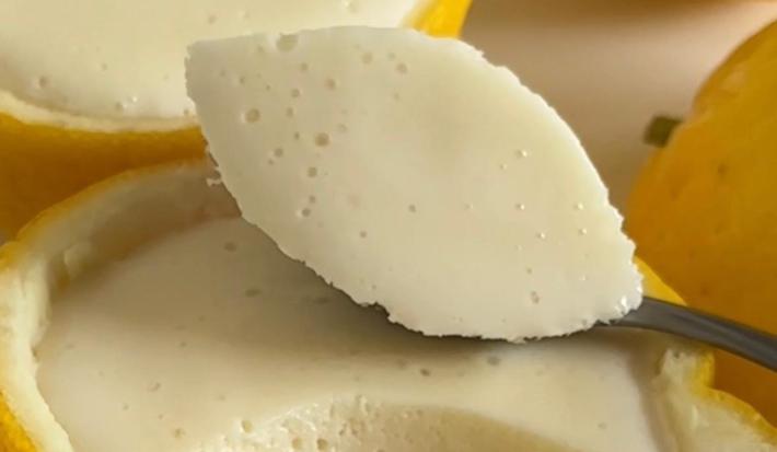 Fotografia de uma receita de mousse de limão siciliano que é servido dentro das cascas do próprio limão. No centro da foto tem uma colher segurando uma porção da mousse.