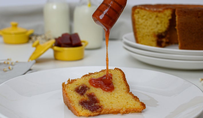 Prato branco com uma fatia de bolo de fubá com goiabada com uma colher derramando calda de goiabada.