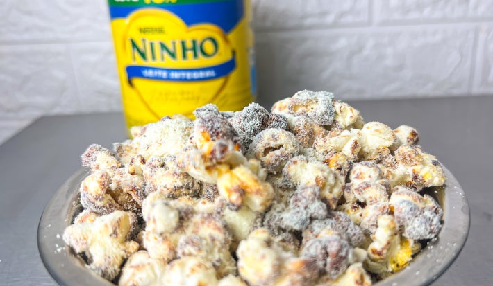 Fotografia em tons claros com um prato de pipoca doce ao centro. As pipocas são cobertas por leite NINHO em pó