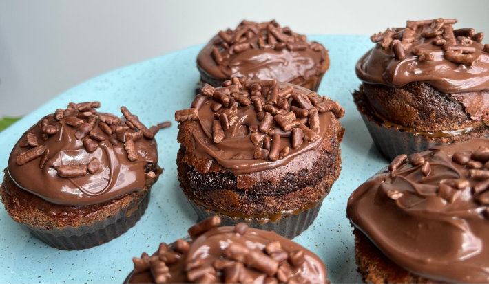 Fotografia mostra seis bolinhos de chocolate coberto por cobertura de chocolate granualdo dispostos em prato azul.