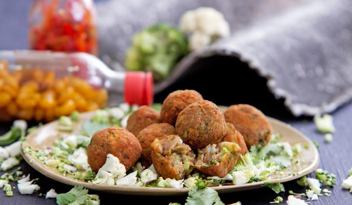 Foto da receita de bolinho de talos, servido em um prato sobre uma bancada cinza com garrafas de pimenta ao fundo