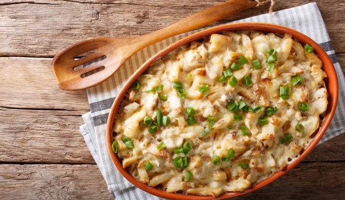 Em cima de uma mesa, recipiente com bacalhau e queijo gratinado, decorado com cebolinha picada.