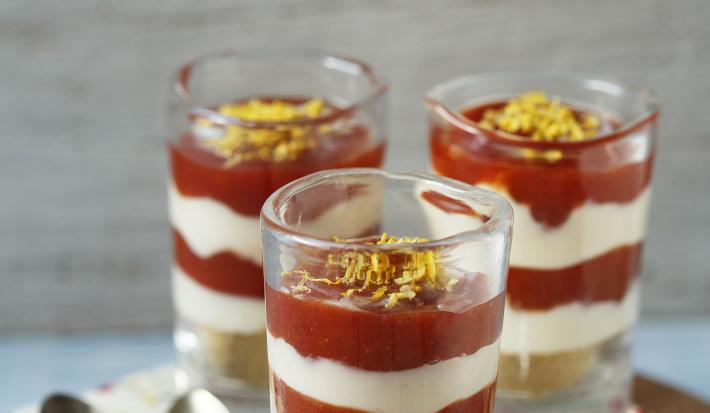 3 copinhos transparentes com Cheesecake de Limão Siciliano e Goiabada. Abaixo uma tábua de madeira redondo com um pano branco florido e 3 colheres para servir.