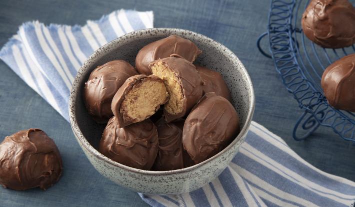 Foto da receita de Bombom de Farinha Láctea NESTLÉ Aveia. Observa-se um recipiente de cerâmica com 7 bombons dentro, sendo que o de cima está cortado ao meio e é possível ver o interior do bombom