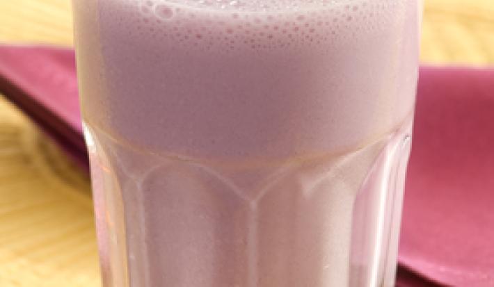 FOTOGRAFIA EM TONS DE MARROM E ROXO. CONTÉM UM COPO TRASPARENTE COM A BEBIBA DE UVA