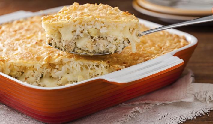 Foto de um refratário laranja com arroz de forno dentro. Há uma colher retirando uma porção do mesmo