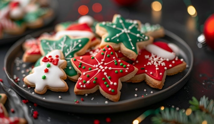 Em cima de uma mesa, prato com biscoitos em formato de estrelas, decorados com glacê colorido e confeitos coloridos de bolinhas verde e vermelho.