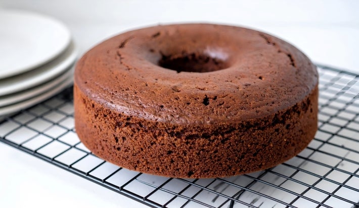 Em cima de uma mesa,  grade com bolo com furo no meio de chocolate fofinho.