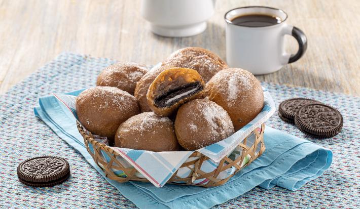 Imagem de uma cesta com bolinhos de chuva recheados com Negresco. Ao lado, biscoitos Negresco e uma xícara de café.