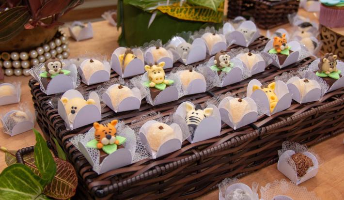 Fotografia de várias forminhas brancas com brigadeiro branco preparado com Leite MOÇA e gema, modelado em formato de animais. As forminhas estão sobre um apoio de madeira trançado.