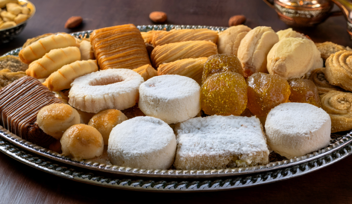 sobre uma mesa de madeira, uma bandeja de prata repleta de doces amanteigados e petit fours em diferentes formatos. Eles são pequenos, dourados, alguns com açúcar, outros com chocolate.