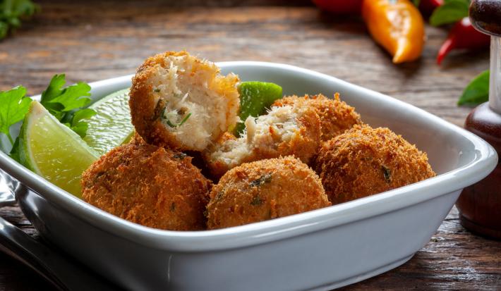 Fotografia em tons de branco com um prato fundo e branco ao centro. Dentro do prato existe vários bolinhos de bacalhau feitos na Air Fryer acompanhados por fatias de limão