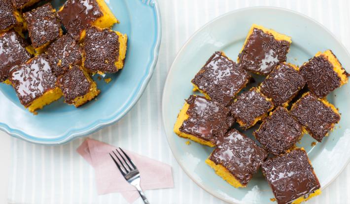 Imagem vista de cima de dois pratos com pedaços quadrados de bolo de cenoura com cobertura de brigadeiro e chocolate granulado.