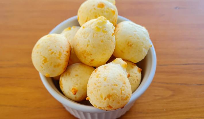 Fotografia de um ramekin branco com vários pães de queijo. O recipiente está sobre uma mesa de madeira.
