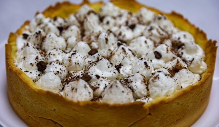 Em cima de uma mesa, banoffee com massa de biscoitos crocante, decorado com chantilly e canela em pó.