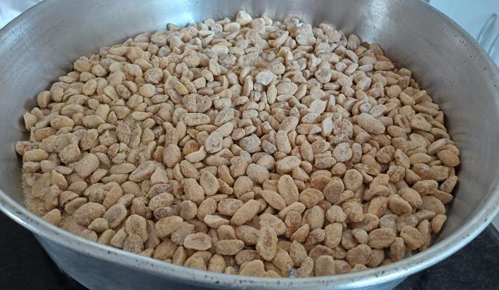 Fotografia de uma panela grande alumínio com amendoins, açúcar e raspas de limão.