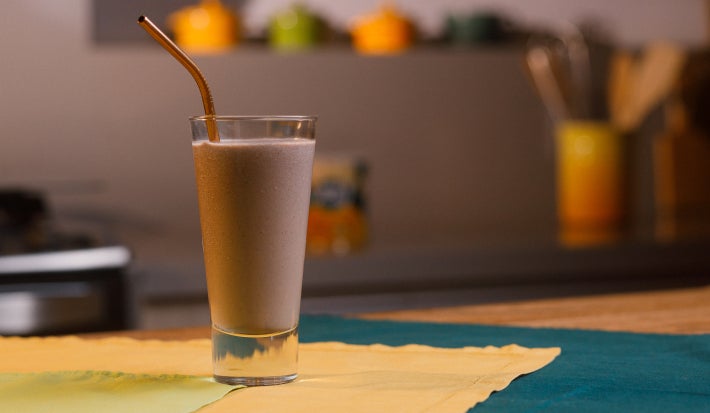 imagem mostra um copo de refresco roxo cremoso preparado com açaí e banana