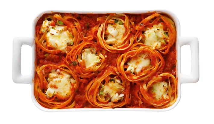 Foto de uma forma branca com 8 macarrão do tipo ninho dentro dela. Todos estão cobertos com molho de tomate e recheados com requeijão e queijo