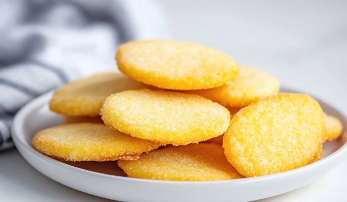 Em cima de uma mesa, prato redondo com biscoitos dourados, polvilhado com açúcar cristal.