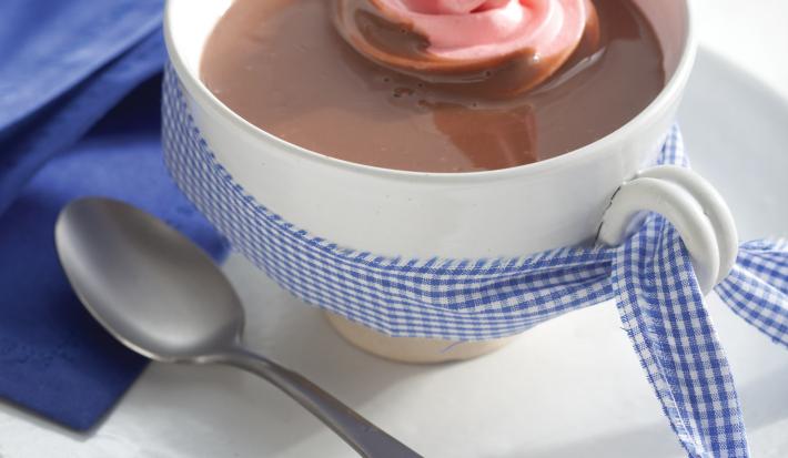 Fotografia em tons de azul em uma bancada de madeira branca com um pano azul ao lado, um prato branco raso pequeno, um xícara branca e o chocolate quente com marshmallow dentro. Fotografia em tons de azul em uma bancada de madeira branca com um pano azul ao lado, um prato branco raso pequeno, um xícara branca e o chocolate quente com marshmallow dentro.