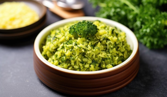 Em cima de uma mesa, um recipiente redondo com porção de arroz soltinho verde, decorado com um brócolis.