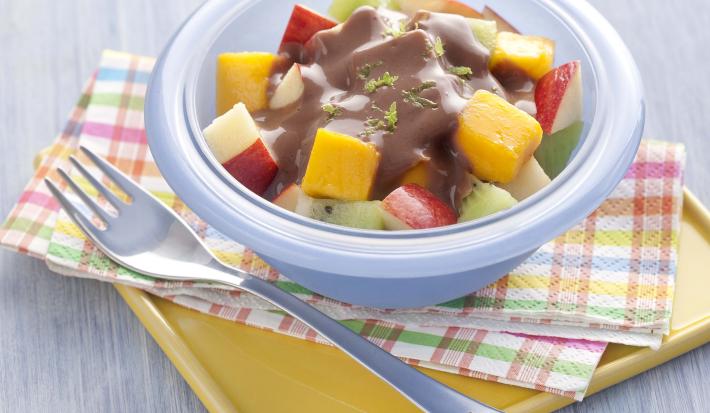 fotografia em tons de azul e cinza de uma bancada cinza vista de cima, contém um pano em tons de rosa, laranja azul e branco, um recipiente redondo e azul com frutas picadas e chocolate com raspas de limão por cima. Ao lado um garfo para servir. fotografia em tons de azul e cinza de uma bancada cinza vista de cima, contém um pano em tons de rosa, laranja azul e branco, um recipiente redondo e azul com frutas picadas e chocolate com raspas de limão por cima. Ao lado um garfo para servir.