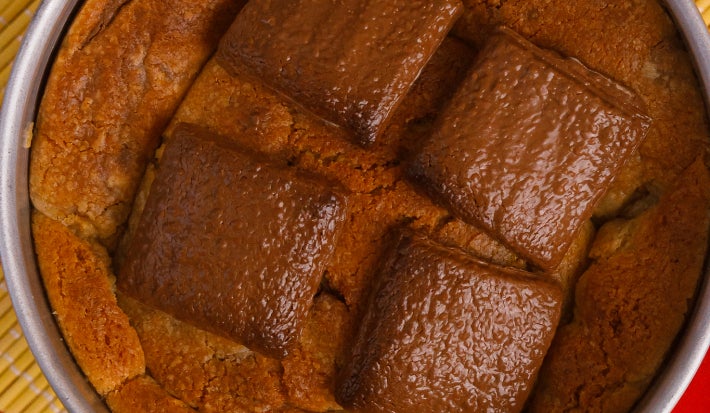 Vista superior de cookie gigante em lata metálica, coberto com pedaços de chocolate Baton.