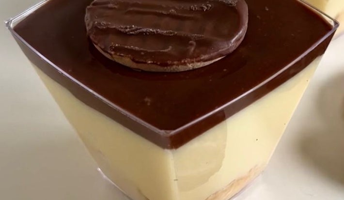Fotografia em tons claros de dois potinhos de plástico quadrados com uma receita de torta holandesa sobre uma mesa branca.